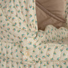 Close-up of the Doll Pram - Fleur Coloré, showcasing a beige quilted fabric adorned with a floral pattern in pink, green, and blue. Made from recycled materials, the fabric is featured in a padded garment with visible button details and stitching, evoking vintage style doll pram designs.