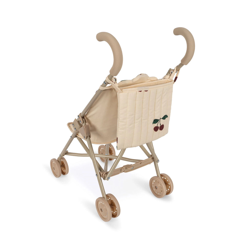 A beige **Konges Sløjd Doll Stroller - Glitter Cherry** with cushioned handles, double wheels, and a padded backrest that features a simple cherry design. The stroller appears compact and lightweight, designed for easy maneuverability and portability.