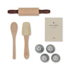 A flat lay of baking tools perfect for tiny bakers includes a wooden rolling pin, a wooden spoon, a beige spatula, a recipe book titled "my recipes, bon appetit," and four metal flower-shaped baking molds. This adorable Madeline Baking Set - Petite Cousine has everything young chefs need to start their culinary adventure.