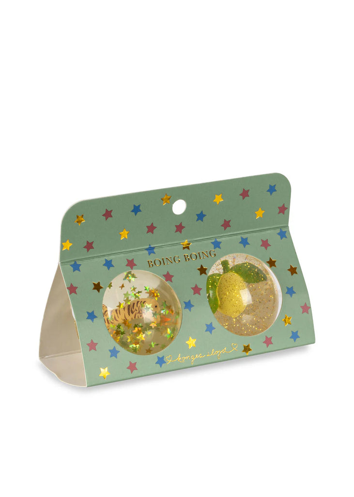 The Konges Sloejd - Bouncing Ball Set includes two transparent bouncing balls filled with colorful confetti. They are packaged in a green triangular cardboard box adorned with a star pattern and circular cutouts that showcase the balls, and "BOING BOING" is printed on the box.