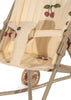 A close-up of the Konges Sloejd Doll Stroller - Grande Cherry Pink Glitter showcases its charming design, with a removable fabric adorned in cherry patterns. The stroller features a secure harness and a glimpse of its wheel, elegantly highlighting its thoughtful design and delightful color theme.