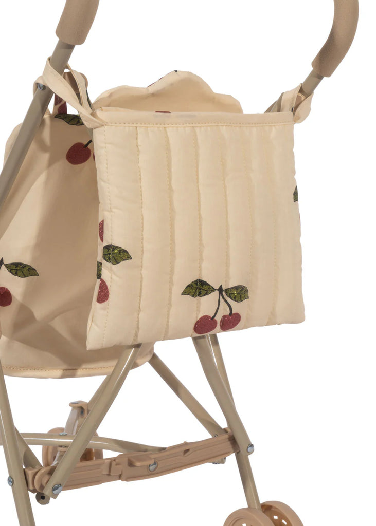 A close-up of the delightful Konges Sloejd Doll Stroller - Grande Cherry Pink Glitter showcases embroidered cherries with green leaves on its quilted, removable fabric. This stroller features a secure harness and a foldable frame.