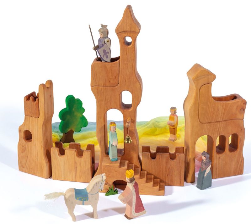 The Ostheimer Lookout - Small is a handcrafted wooden castle playset featuring hand-painted figures, including a knight, king, queen, and other characters in medieval attire. This castle includes towers, archways, and walls, along with a horse figure and a green felt tree. It creates a bright and colorful scene perfect for imaginative play.