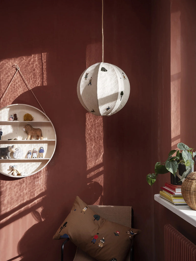 A cozy corner of a room with terra cotta walls, featuring a spherical pendant lamp adorned with floral patterns, hanging above a plush cushion with embroidered designs. A wall-mounted Ferm Living Round Hanging Shelf crafted from beech.