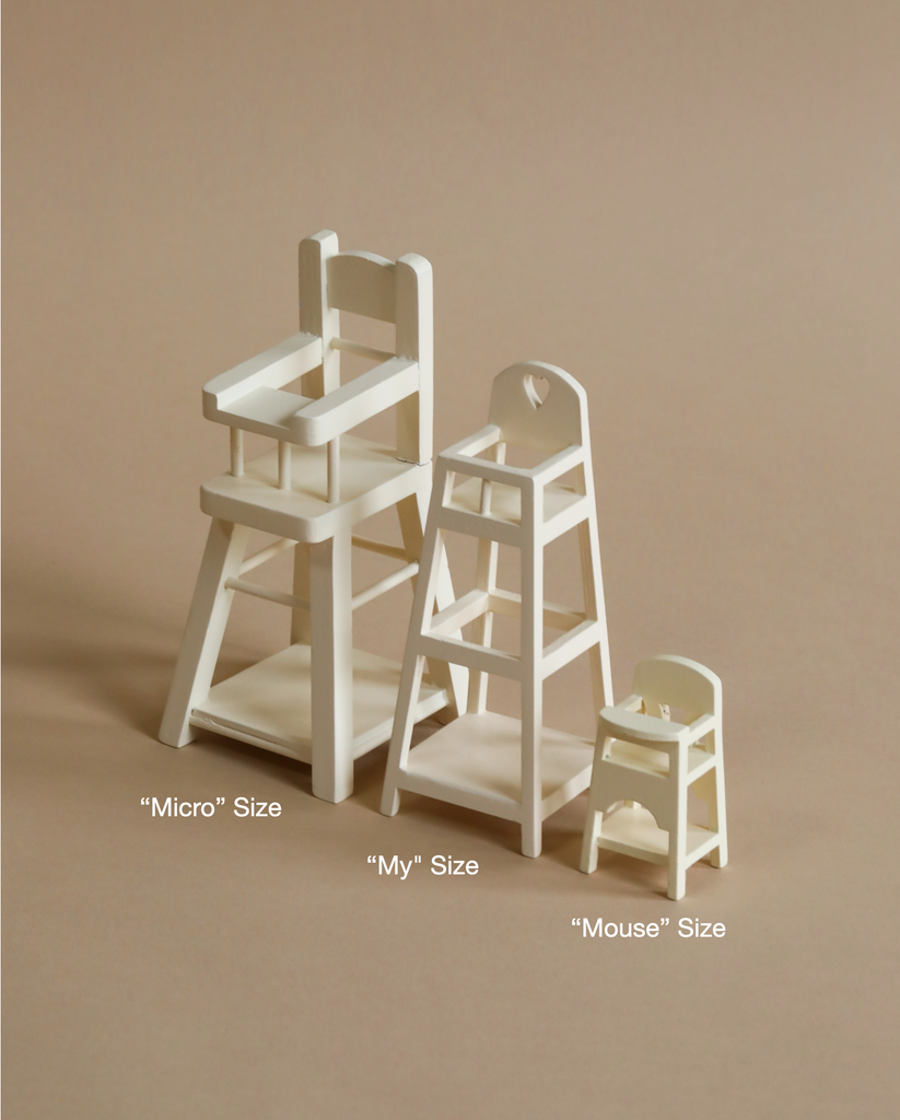 Three miniature, white wooden high chairs are lined up on a beige background. The baby high chairs are labeled from left to right: "Micro" Size, "Maileg My High Chair," and "Mouse" Size, decreasing in size accordingly. These charming pieces make perfect nursery furniture.