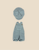 A set of light blue, pinstriped baby clothes on a plain background. The outfit, found in the Maileg Extra Clothing: Overall and Cap for Teddy Junior collection, features a pair of overalls with a large front pocket and two brown buttons on the straps, along with a matching round and slightly puffed hat.