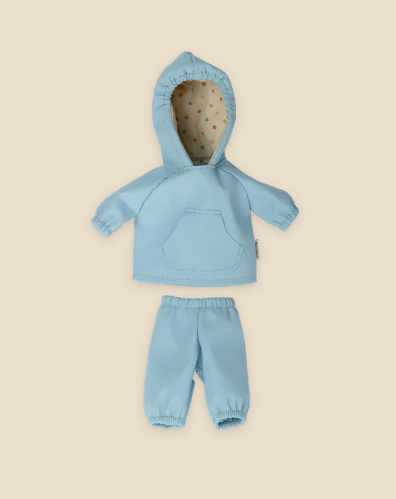 Introducing the Maileg Extra Clothing: Rainwear for Teddy Junior - a delightful blue hooded jacket with a pocket, paired with matching blue pants, designed as an ideal outfit for Teddy Junior or any cherished doll. The inner lining of the hood boasts a dotted design, all beautifully showcased on a light beige background.