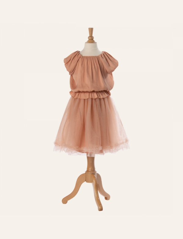 A Maileg Princess Blouse - Melon (Final Sale) displaying a peach-colored dress with ruffled sleeves, a gathered bodice, and a tulle skirt, as if plucked from a fairytale dream. The mannequin stands on a wooden tripod base against a plain, light background.