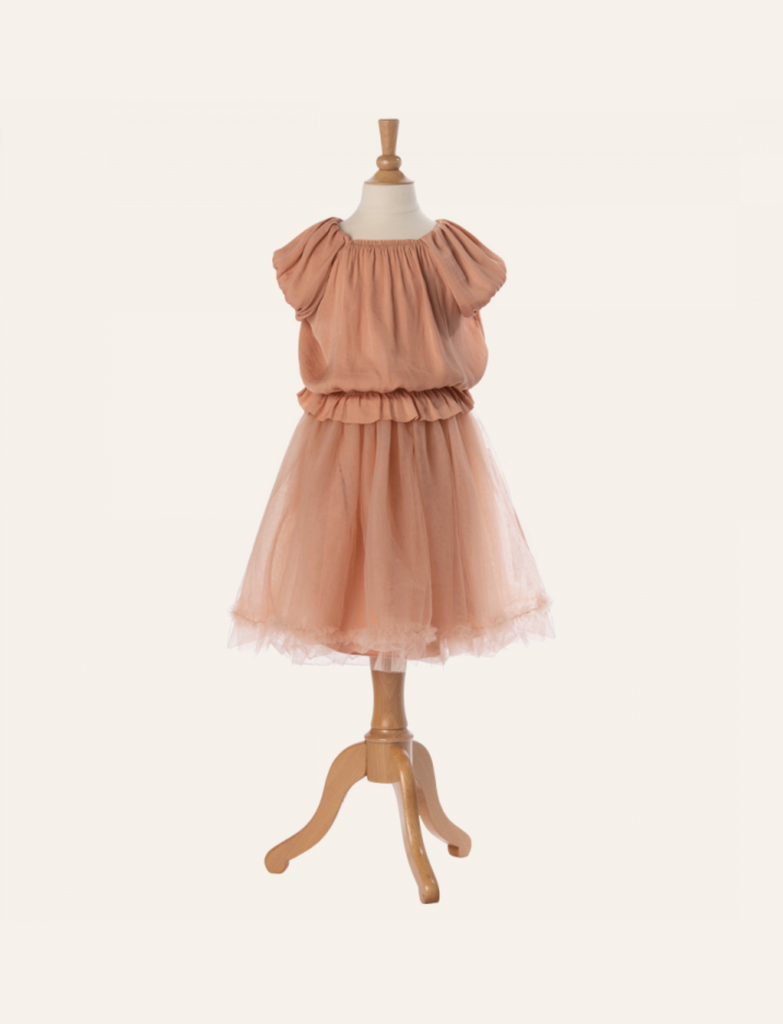 A Maileg Princess Blouse - Melon (Final Sale) displaying a peach-colored dress with ruffled sleeves, a gathered bodice, and a tulle skirt, as if plucked from a fairytale dream. The mannequin stands on a wooden tripod base against a plain, light background.