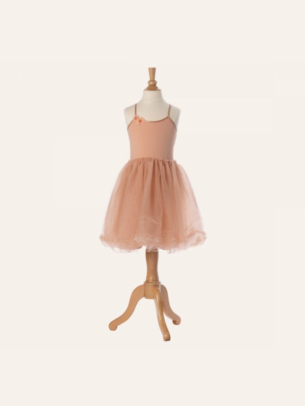 A peach-colored Maileg Princess Tulle Dress - Melon displayed on a wooden mannequin evokes a fairytale dream. The dress, composed of soft materials, features a fitted bodice with thin straps and a flared, tulle skirt. Set against a plain, light beige background, it looks like an enchanting piece from a Magical Wardrobe.