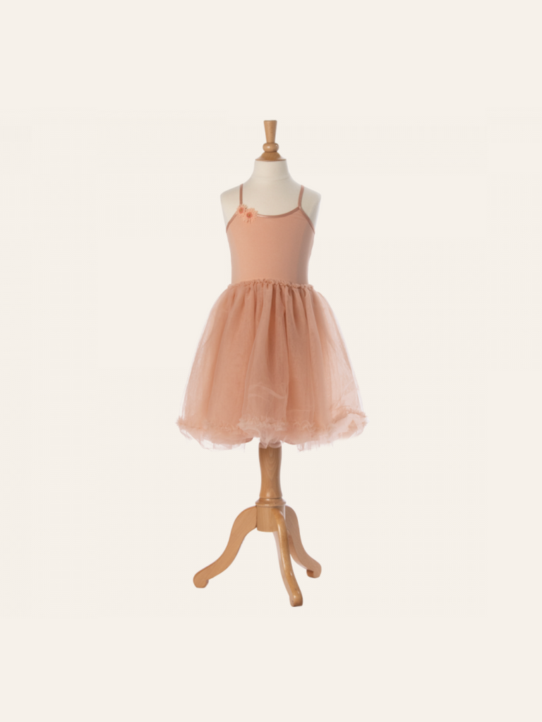 A peach-colored Maileg Princess Tulle Dress - Melon displayed on a wooden mannequin evokes a fairytale dream. The dress, composed of soft materials, features a fitted bodice with thin straps and a flared, tulle skirt. Set against a plain, light beige background, it looks like an enchanting piece from a Magical Wardrobe.