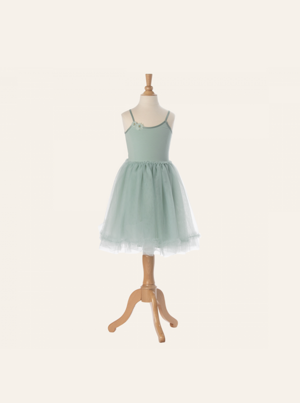 A pastel green, sleeveless tutu dress for children is displayed on a wooden mannequin. This Maileg Princess Tulle Dress - Mint features a fitted bodice with a delicate flower detail on one strap and a full tulle skirt that adds volume. The background is neutral, emphasizing the magical wardrobe piece.