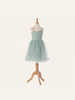 A pastel green, sleeveless tutu dress for children is displayed on a wooden mannequin. This Maileg Princess Tulle Dress - Mint features a fitted bodice with a delicate flower detail on one strap and a full tulle skirt that adds volume. The background is neutral, emphasizing the magical wardrobe piece.