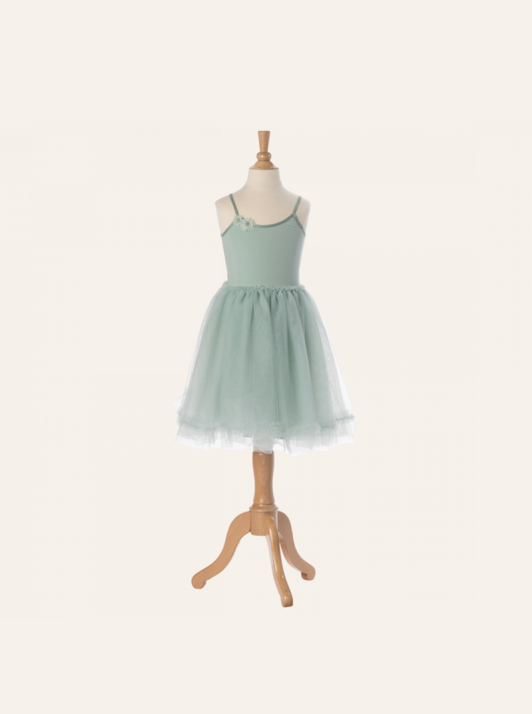 A pastel green, sleeveless tutu dress for children is displayed on a wooden mannequin. This Maileg Princess Tulle Dress - Mint features a fitted bodice with a delicate flower detail on one strap and a full tulle skirt that adds volume. The background is neutral, emphasizing the magical wardrobe piece.