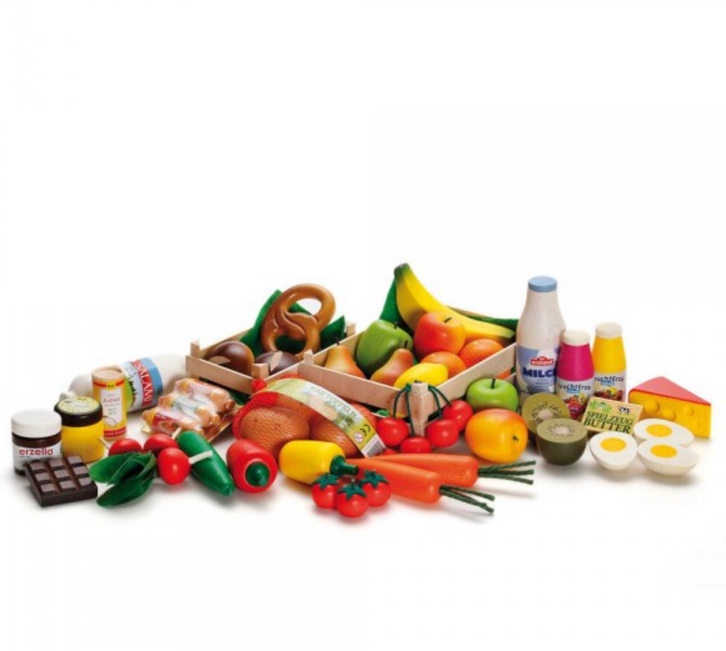 A variety of toy food items are displayed, including wooden pieces like apples and bananas, vegetables like carrots and tomatoes, dairy products such as milk bottles, bread, chocolate, eggs, and various packaged goods. This Erzi Big Box of Play Food Shop Assortment is perfect for a pretend play store. Items are arranged on a white background.