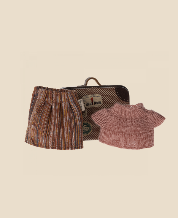 An image shows a small metal suitcase adorned with various travel stickers, accompanied by a knitted holiday toy consisting of a brown striped skirt and a pink short-sleeved top, both intricately detailed. The skirt has a drawstring waist, and the suitcase has a handle on top. This product is called Maileg Knitted Blouse And Skirt In Suitcase, Grandma Mouse.