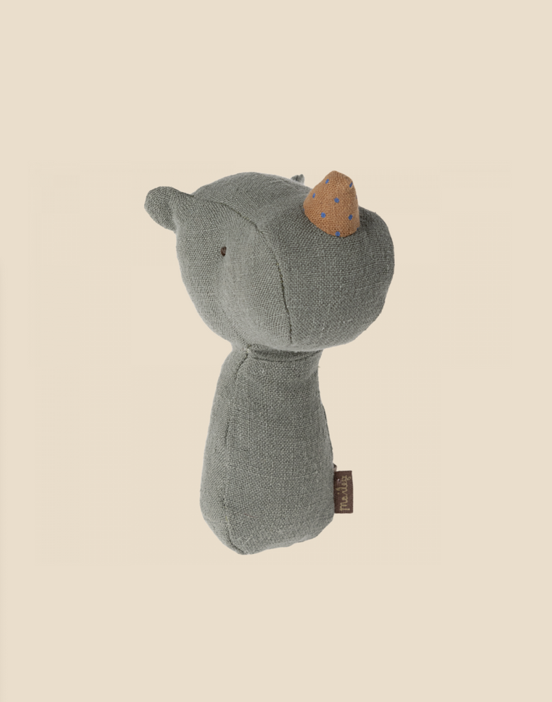 A small, stuffed animal toy resembling a bear stands against a beige background. The toy is made of grey fabric with a brown snout featuring blue polka dots and small, sewn-on eyes. A brown tag is attached to its side. This adorable piece makes a perfect gift for babies and comes tucked in a charming gift box.

Product Name: Maileg Lullaby Friend Rattles, Rhino - Pine