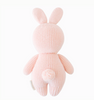 A Cuddle + Kind Baby Rabbit, Powder Pink, crafted from heirloom-quality natural Peruvian cotton yarn, is shown from the back. The toy has long ears, a round body, short arms and legs, and a small fluffy tail at the bottom. The texture of the hand-knit fabric is clearly visible.