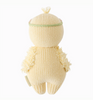 The image shows the back view of a Cuddle + Kind Baby Duckling, Blush Floral, crafted from soft Peruvian cotton yarn, with a green band on its head. The texture is fluffy around the wings. The tail is short, and the overall appearance is round and cuddly, making it an heirloom-quality keepsake.