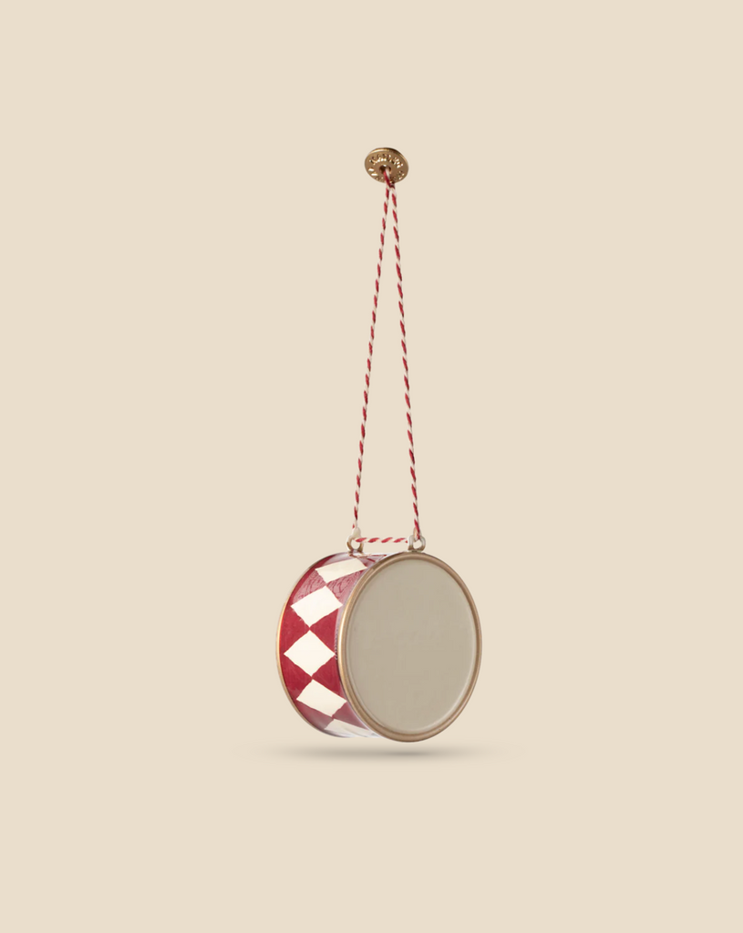 A Maileg Metal Ornament, Large Drum - Red, featuring handpainted details with a red and white diamond pattern, hangs from a twisted red and white cord against a plain beige background.