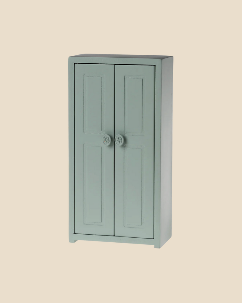 A small, soft blue wooden Maileg Mouse Closet, with two paneled doors each adorned with a round knob, stands daintily against a beige background. It's charming enough to serve as a cozy little closet for a mouse family. (Ships in approximately one week.)