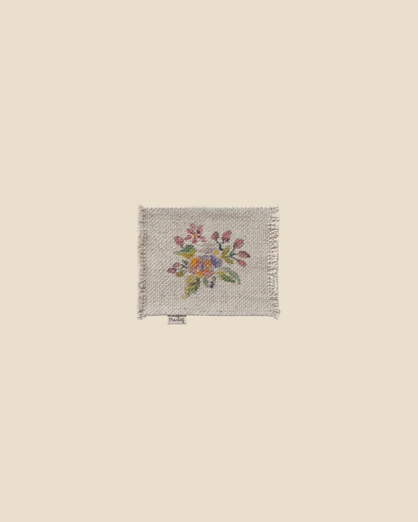 The Maileg Flower Rug, Small features a charmingly rustic look with its textured cotton fabric and embroidered design of vibrant flowers in shades of red, yellow, and green set against a simple beige background. The slightly frayed edges enhance its appeal.