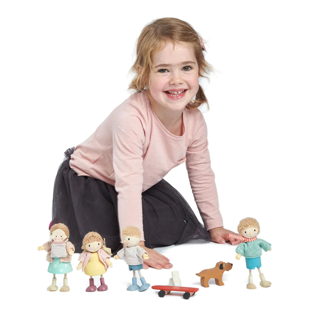 A young girl with a joyful expression plays on the floor with Mrs. Goodwood and her Baby, all crafted from solid wood. She wears a pink top and dark pants, positioned on her knees and leaning