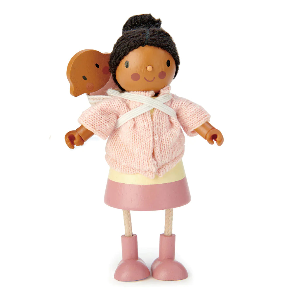 A wooden doll with dark skin and black hair styled in knotted buns, wearing a pink sweater, white scarf, and pink skirt made of knitted fabrics, holds Mrs. Forrester and the Baby.