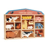 A wooden display shelf shaped like a barn, labeled "farmyard animals," containing various colorful wooden animal figures such as a cow, pig, chicken, and more. This plastic-free toy is made from Farmyard Animals Set.