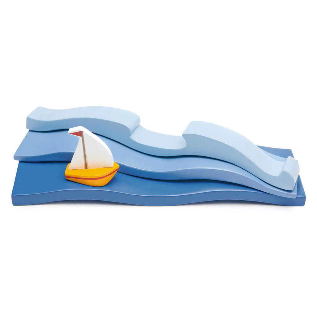 A Blue Water and Sail Boat Set featuring three blue wavy pieces stacked to resemble waves and a small yellow sailboat with a white sail positioned on the waves. The design is simple and colorful, evoking a playful nautical theme perfect for open-ended play.