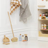 A children's playroom scene features the Pretend Play Cleaning Set and kitchen items, including a toy broom, dustpan, bottles, cans, and towels on hooks against a white wall. A toy shelf holds pretend pantry items made from FSC-certified wood for safe play.