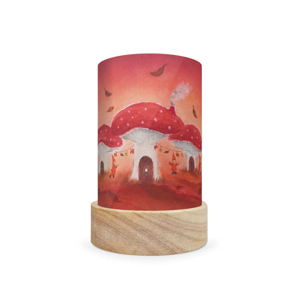 The Toverlux Lantern Shade Set - Seasons by Baukje Exler features a cylindrical lamp design with a wooden base, adorned with an enchanting illustration of red-capped mushrooms with white spots. The backdrop of a warm orange sky includes falling leaves and tiny figures climbing the mushrooms, creating a magical aesthetic. It is available for shipping in approximately one week.