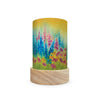 The Toverlux Lantern Shade Set - Seasons by Baukje Exler, featuring a cylindrical table lamp with a wooden base, highlights a vibrant watercolor design of wildflowers. Enchanting shades of pink, purple, and blue blossoms are vividly displayed against a gradient backdrop of yellow and green. This product ships in approximately one week.