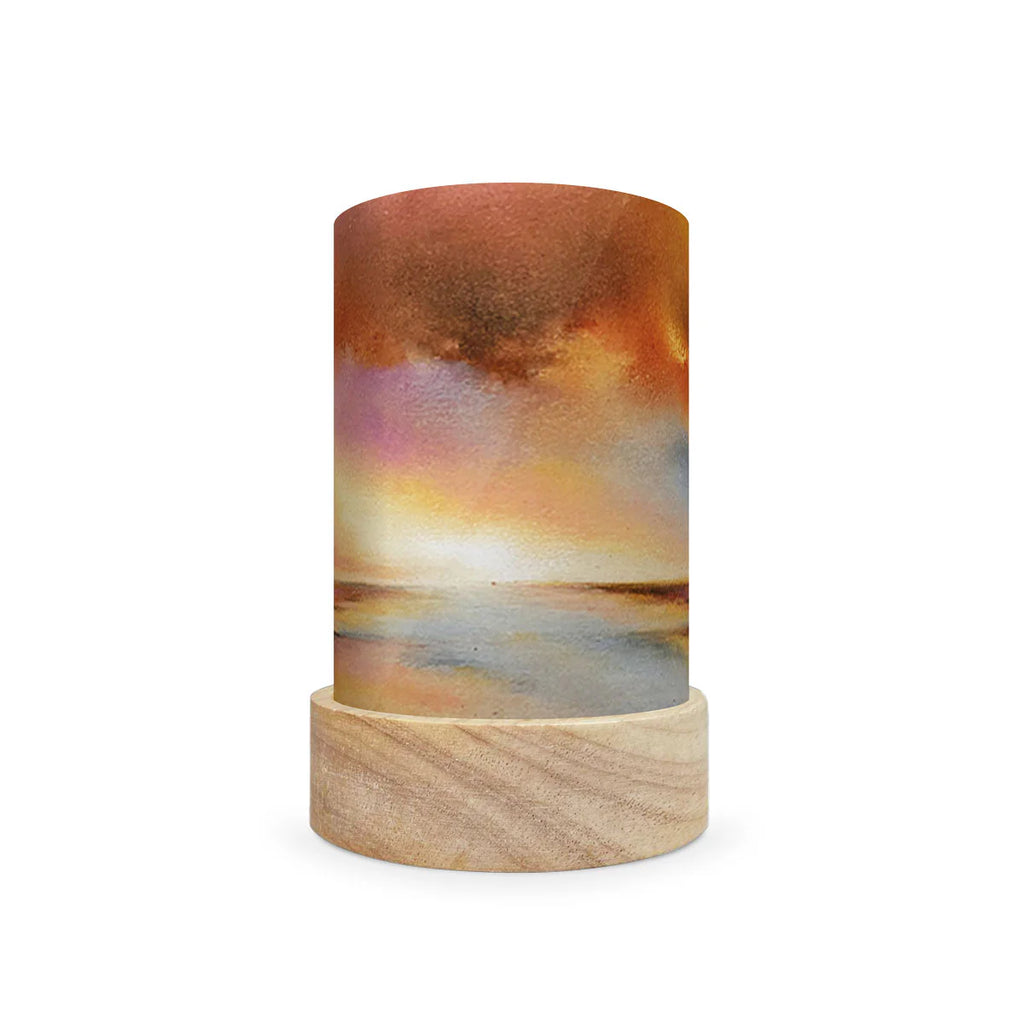 The Toverlux Lantern Shade Set - Holidays features a cylindrical candle with an abstract design depicting a vibrant sunset over a calm sea, accented by lantern silhouettes and elegantly set on a wooden base. Shipping is available in approximately one week.