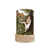 The Toverlux Lantern Shade Set - Robin Pieterse beautifully depicts a woman with braided hair sitting by a tree, holding a basket and gazing at a bird. Behind her is a charming house surrounded by trees and flowers, complete with two birds on the grass. This decorative piece is elegantly arranged with its wooden base.