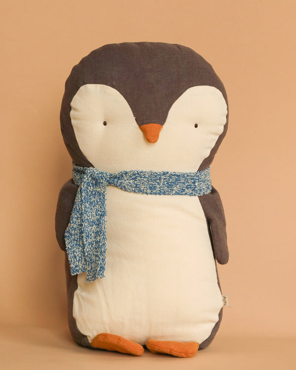 The Maileg Penguin Stuffed Animal - Medium is a soft and plush toy made from gentle fabrics, showcasing a light brown head and flippers, a white belly, and an orange beak and feet. It comes with a stylish blue knit scarf set against its light brown features, making it an ideal choice for all ages.