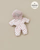 Discover the cozy Gigi Pink and White Checkered Ski Suit for Minikane Gordis dolls. Featuring a charming light pink and white pattern, this jumpsuit is equipped with a fluffy hood, zip-up front, and cinched waist for an adorable fit. A circular label on the top right specifies it "fits MINKANE 13'' & 14''." The solid beige background sets the perfect scene for any winter adventure with your doll.