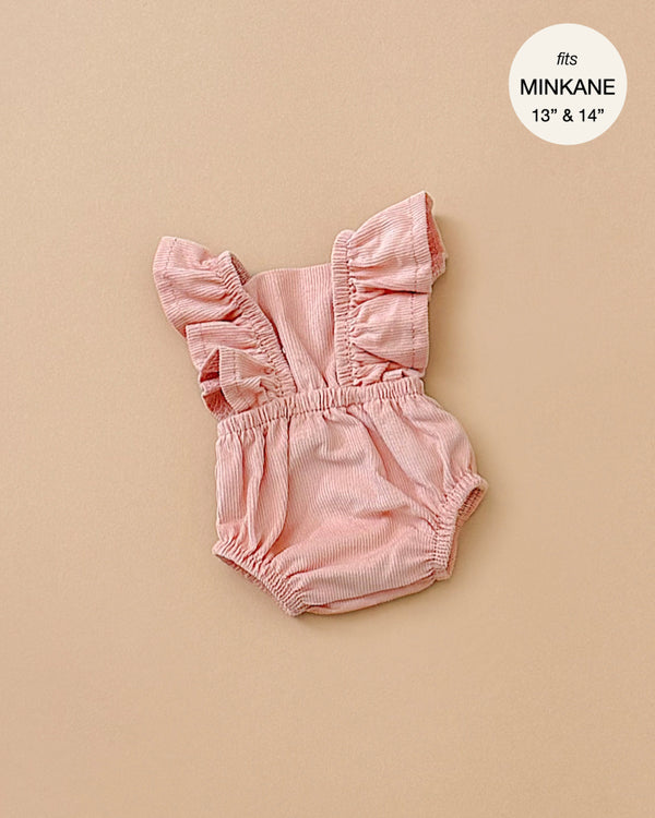 Displayed on a beige background, the Lou Retro Romper in Salmon Corduroy is a pink, ruffled doll romper ideal for Minikane dolls. Designed to fit 13" and 14" dolls, this stylish piece is created in France and is conveniently hand washable.