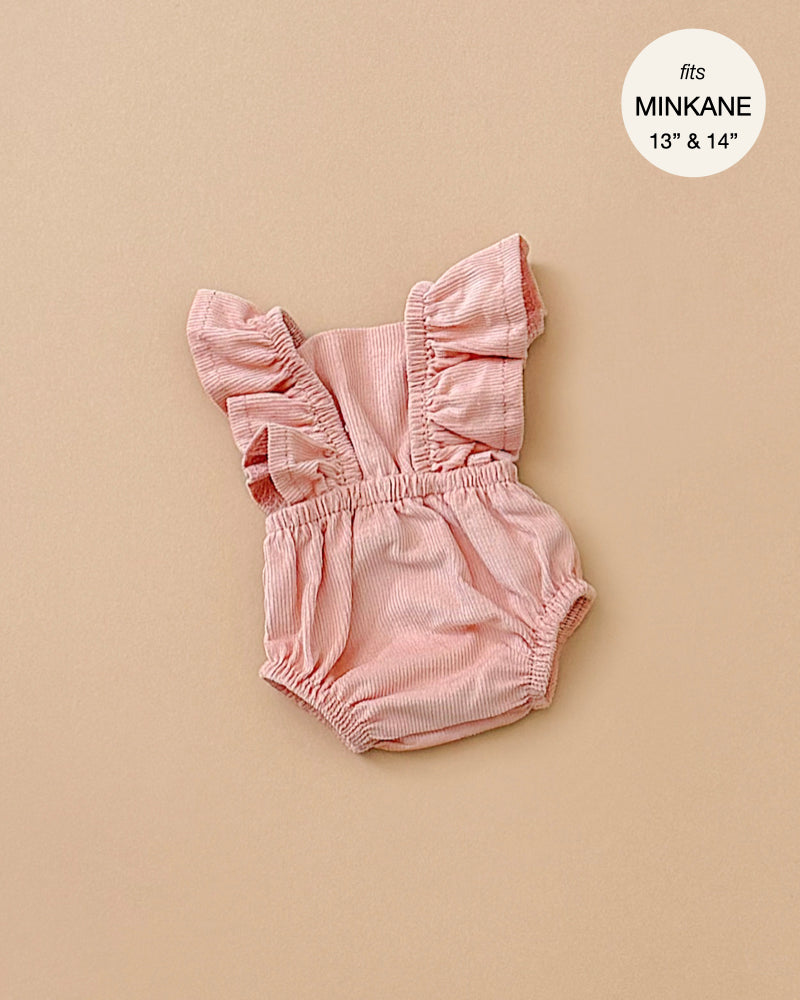 Displayed on a beige background, the Lou Retro Romper in Salmon Corduroy is a pink, ruffled doll romper ideal for Minikane dolls. Designed to fit 13" and 14" dolls, this stylish piece is created in France and is conveniently hand washable.