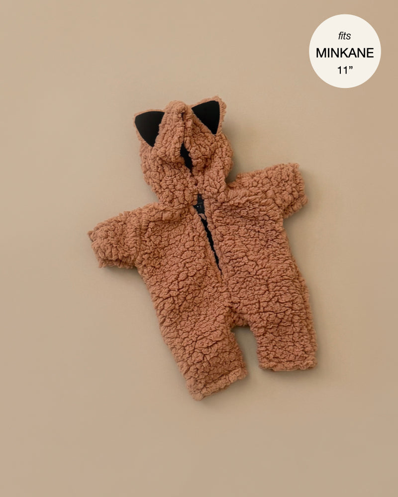 A Minikane Doll Clothing Brown Sugar Sherpa Costume, a small fleece onesie with brown teddy bear design and black ear accents, is laid flat on a beige background. The text overlay reads "fits Minikane babies 28cm dolls.