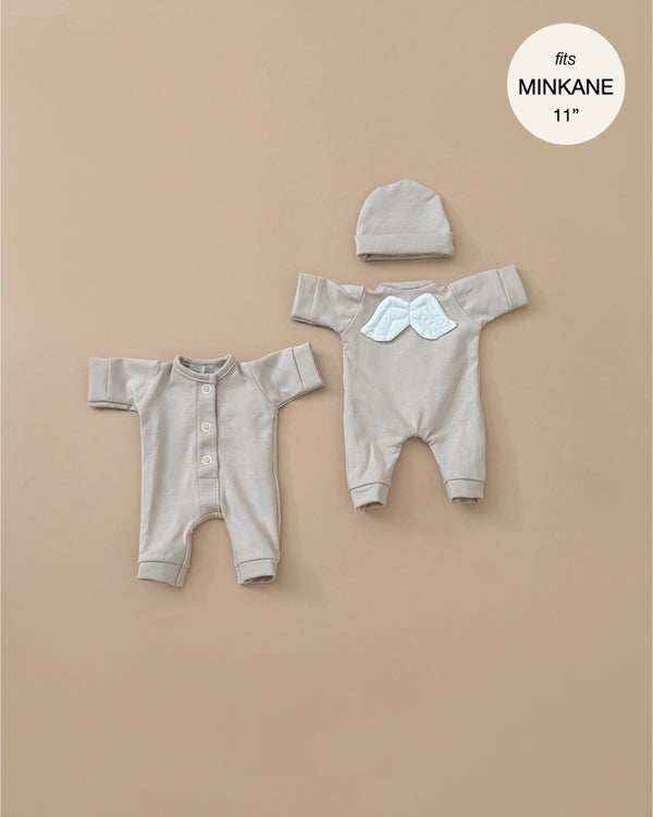 Displayed on a neutral background are two beige baby outfits: a buttoned jumpsuit and a onesie with cloud detail, accompanied by a matching hat. A note reads, "fits Minikane 11\" babies," making them ideal for those who cherish French-inspired doll fashion. These outfits are part of the "Little Angel" Linen Jersey collection from Minikane Doll Clothing.