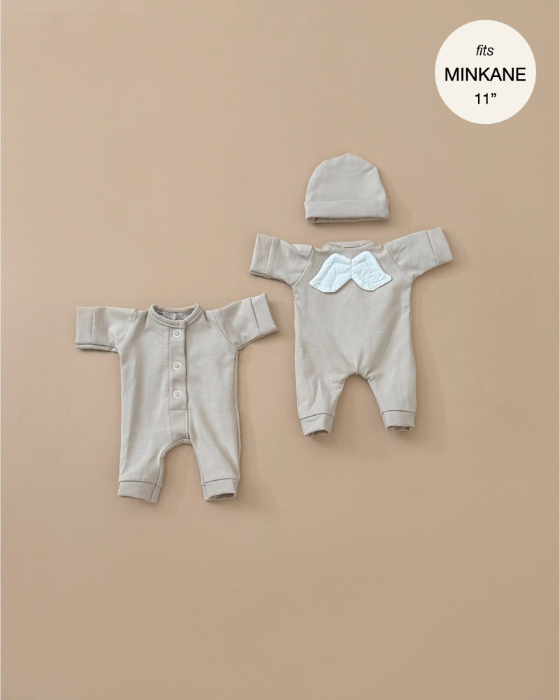 Displayed on a neutral background are two beige baby outfits: a buttoned jumpsuit and a onesie with cloud detail, accompanied by a matching hat. A note reads, "fits Minikane 11\" babies," making them ideal for those who cherish French-inspired doll fashion. These outfits are part of the "Little Angel" Linen Jersey collection from Minikane Doll Clothing.