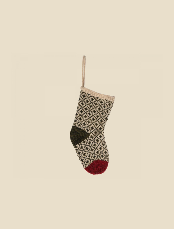 The Maileg Christmas Stocking - Green is a decorative knitted stocking featuring a green and red color scheme with intricate patterns of diamonds and crosses. It comes with a beige loop for hanging and includes a red toe, a green heel, and a beige cuff at the top, making it perfect for holding small gifts.