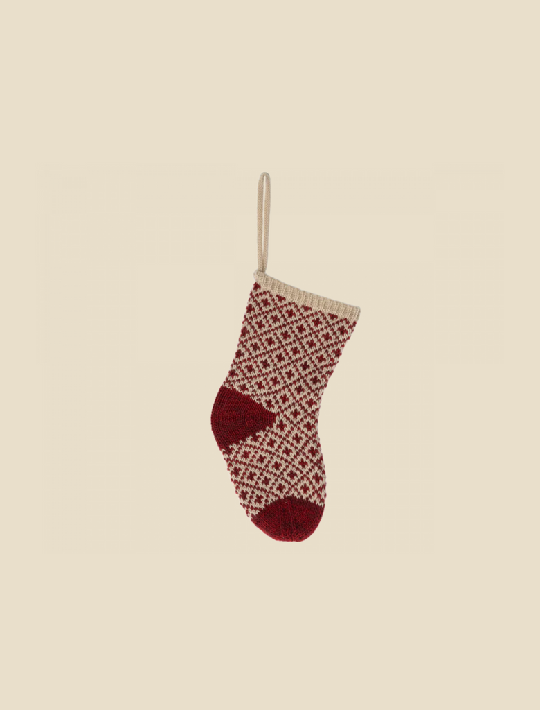 The Maileg Christmas Stocking - Red hangs by a beige loop against a light background, showcasing its red and white geometric pattern. Perfect for small gifts, the stocking features a red heel and toe, complemented by a light beige cuff.