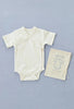 A cream-colored Baby Romper with a wrap-style front and snap buttons is placed on a light gray background. Beside it is a beige drawstring cloth bag with an illustration of a romper and the text "baby romper" printed on it. Machine wash for easy care.
