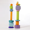 Two towers of vibrant, non-toxic Grimm's Tree Slices Building Blocks are stacked against a white background. The shapes include hexagons, rectangles, and cylinders in bright colors such as orange, green, blue, purple, and yellow. Perfect for young children to explore playful and balanced arrangements.