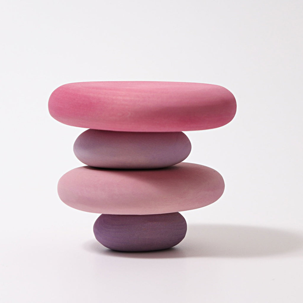 A minimalist stack of four smooth, rounded stones in gradient shades of pastel pink and lavender, balanced on a white surface against a plain white background, these Grimm's Flamingo Pebbles Stacker double as non-toxic toys perfect for a serene balance game.