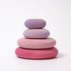 A minimalist stack of four smooth, round wooden discs in shades of pink and purple, arranged from largest at the bottom to smallest at the top, sits against a plain white background, resembling stacking pebbles. These non-toxic Grimm's Flamingo Pebbles Stacker toys make for a delightful balance game.