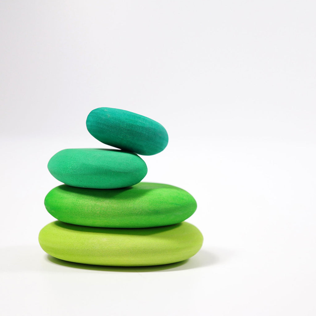 Four smooth, oval-shaped stones painted in various shades of green are stacked on top of each other against a plain white background. The Moss Pebbles Stacker balances precariously, creating a visually appealing and minimalistic composition.