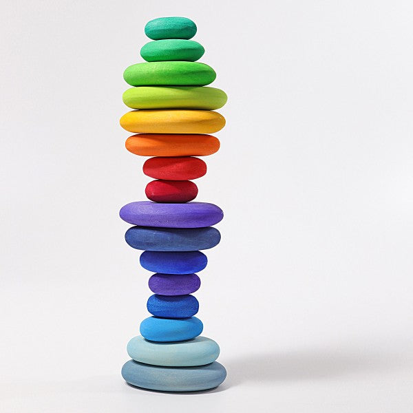 The Grimm's Dream Pebbles Stacker features a tall and narrow tower of flat, smooth stones arranged in a gradient pattern, transitioning from blue at the bottom through purples, reds, oranges, yellows, and ending with green at the top. The non-toxic color stain highlights the organic stone shapes stacked in an almost symmetrical order.